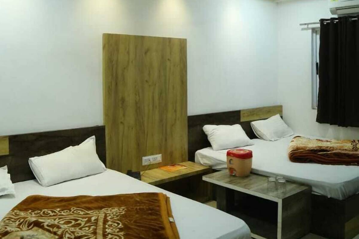 A hotel room with two beds, a wooden headboard, a small table with a lamp, and a ceiling fan.