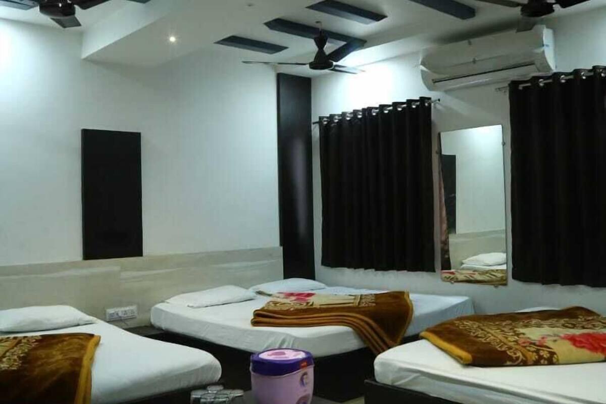 A modern hotel room with three beds, a black nightstand, a ceiling fan, and a large mirror.