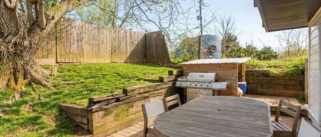 An outdoor patio with a wooden table and chairs, a grill, and a wooden fence.