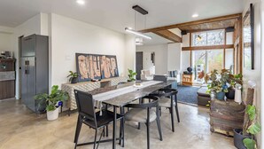 A modern kitchen with a dining area, featuring a long table, chairs, and a large window with natural light. - Modern 5BR Home with Mtn Views, BBQ & Pool Table (Asheville)