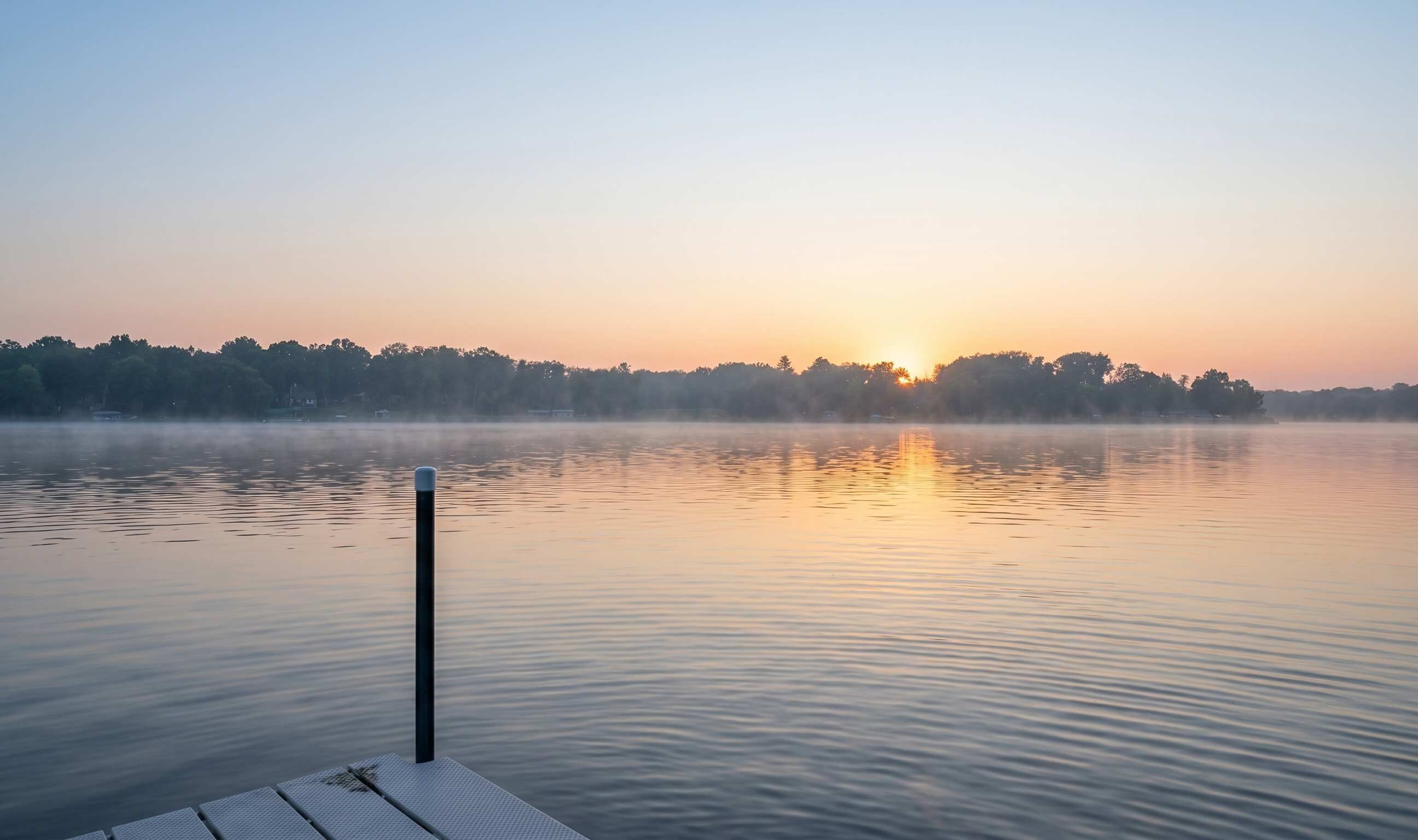 A calm lake at sunrise with a dock extending into the water.