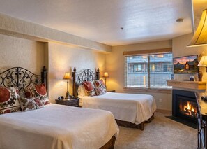 Ein Hotelzimmer mit zwei Betten, einem Kamin und einem großen Fenster mit Blick auf die Stadt.