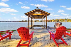 A wooden pier with two red Adirondack chairs facing a gazebo over a body of water.