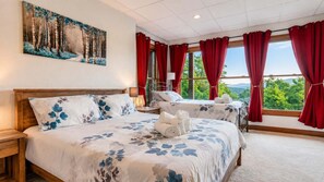 Une chambre d’hôtel avec un grand lit, un lit plus petit, un tableau au mur et une vue sur l’extérieur par les fenêtres.