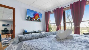 Un dormitorio con una cama grande, un cuadro de globos aerostáticos y vistas del exterior a través de la ventana.