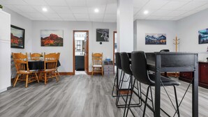 Habitación de hotel con comedor que incluye una mesa y sillas de madera, un escritorio de metal negro y obras de arte en las paredes.