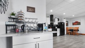Una cocina moderna con armarios blancos, una zona de café y un comedor con sillas de madera.