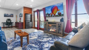 Una sala de estar con chimenea, un sofá, una mesa de centro y un ventanal con cortinas.