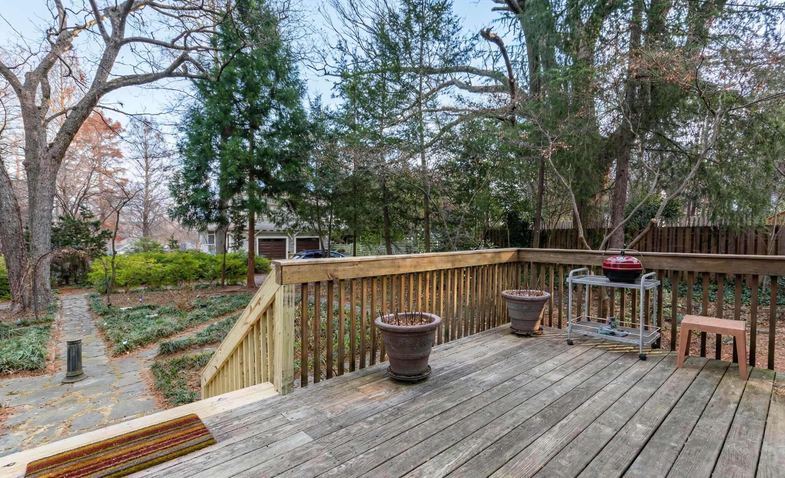 Une terrasse en bois avec une rambarde, des plantes en pot, un barbecue et une petite table.