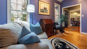 A living room with a sofa, blue pillows, a wooden chest of drawers, and a framed picture on the wall.