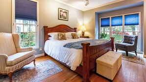 A bedroom with a wooden bed, a chair, a small ottoman, and a nightstand with a lamp.