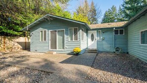 Une maison de plain-pied avec un porche à l’avant, un garage et une petite cour recouverte de gravier, où se trouve un pot de fleurs.