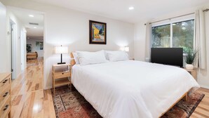 Une chambre à coucher avec un grand lit, deux tables de chevet avec des lampes, un tableau au mur et une fenêtre avec des rideaux.