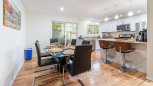 Une cuisine moderne avec un coin repas, comprenant une table à plateau en verre, des chaises noires et une poubelle bleue.