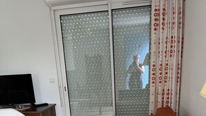 Ein Zimmer mit einer Couch, einem Fernseher auf einem Schrank, einem Tisch und einer Schiebetür mit satinierten Glasscheiben.