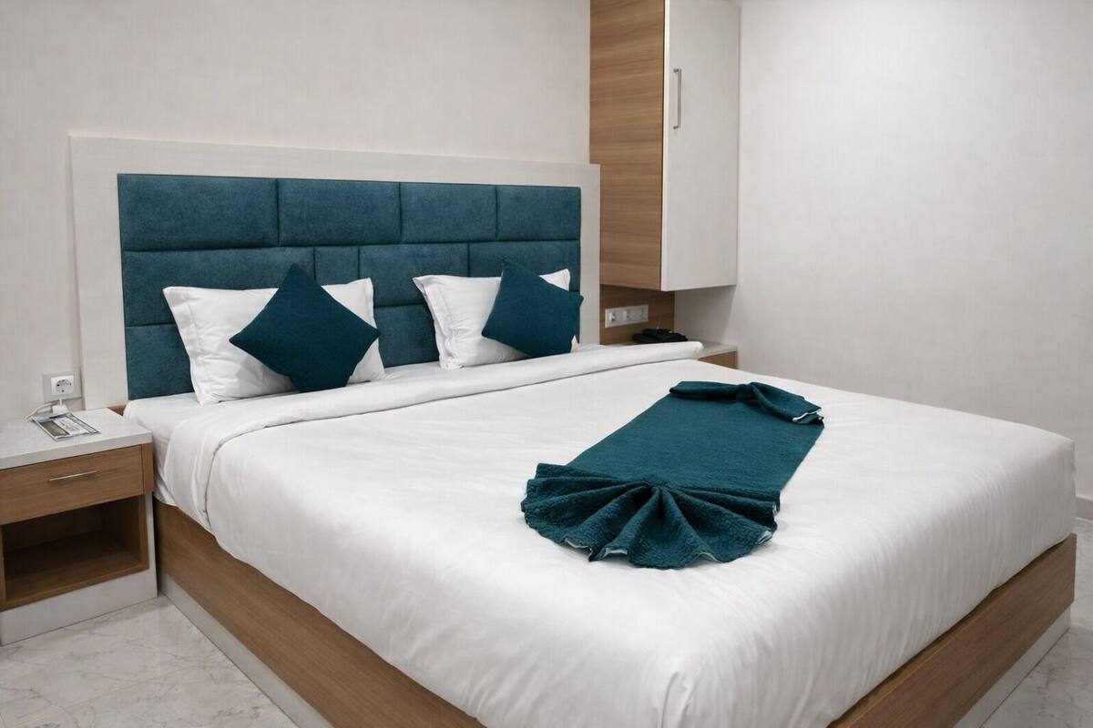 A neatly made bed with a teal throw blanket, white bedding, and a blue upholstered headboard.