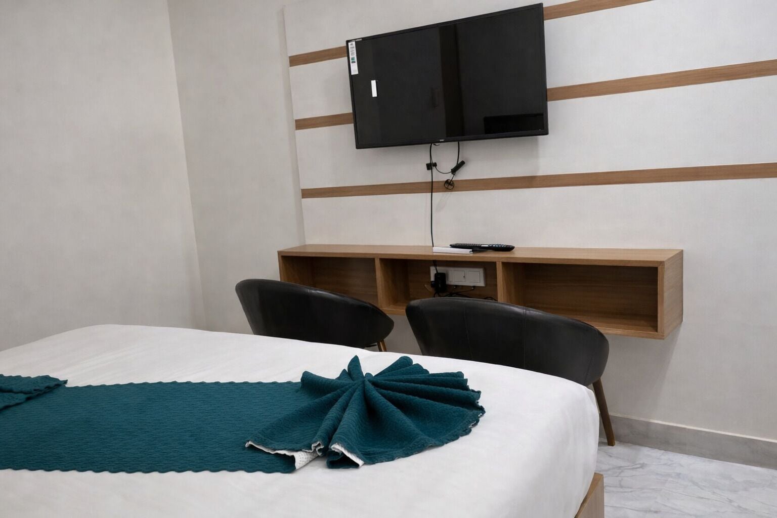 A hotel room with a bed, two chairs, a desk, a television, and a wooden shelf.