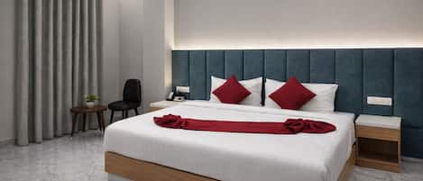 A modern hotel room with a large bed, two bedside tables, a chair, and a desk.