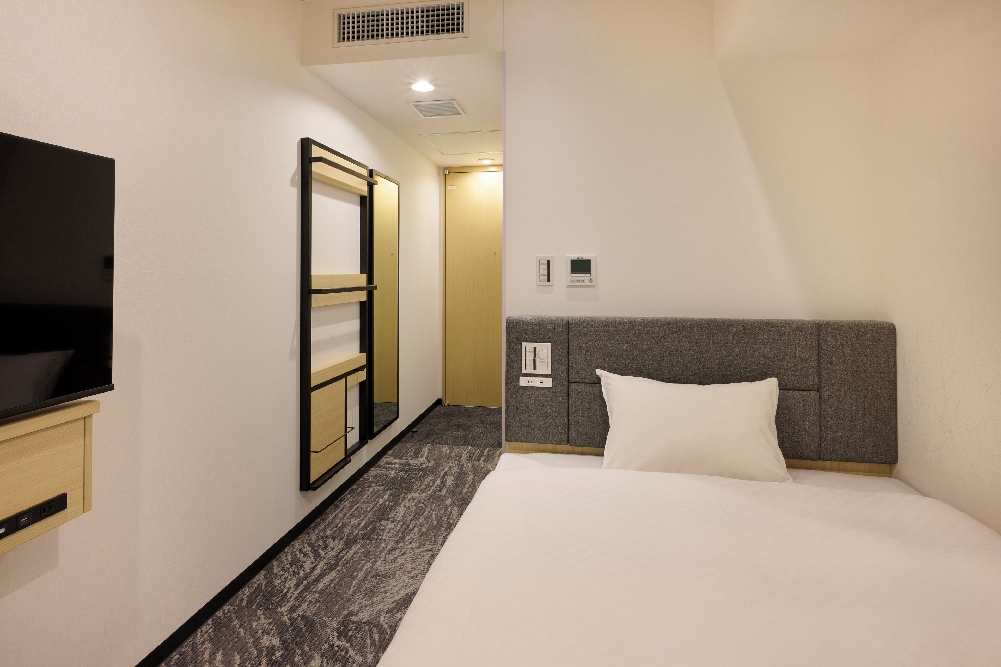A hotel room with a bed, a TV, a wardrobe, and a door leading to another room.