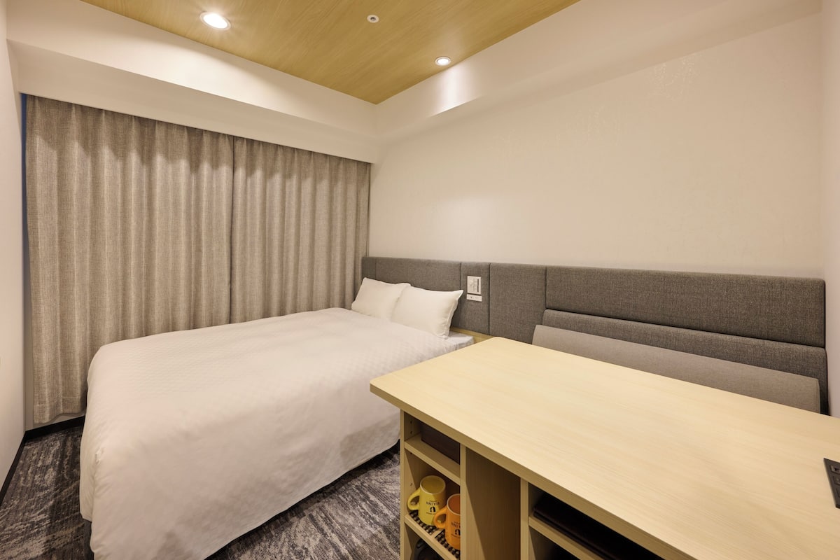 A hotel room with a bed, a desk, and a headboard.