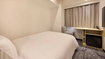 A hotel room with a bed, a desk, a chair, a small refrigerator, and a window with curtains.