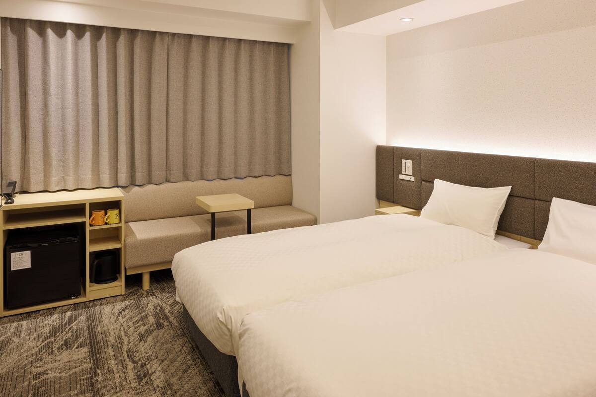A hotel room with a large bed, a desk, a chair, a small table, and a minibar.