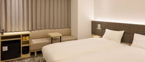 A hotel room with a large bed, a desk, a chair, a small table, and a minibar.