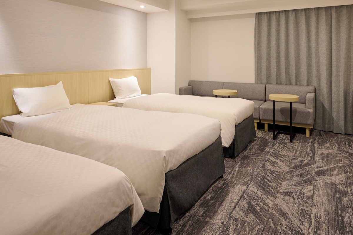 A hotel room with three beds, a sofa, and two small tables.