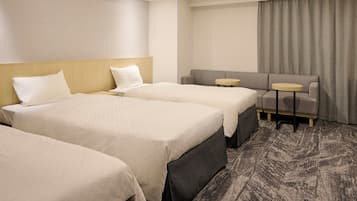 Una habitación de hotel con tres camas, un sofá y dos mesitas.