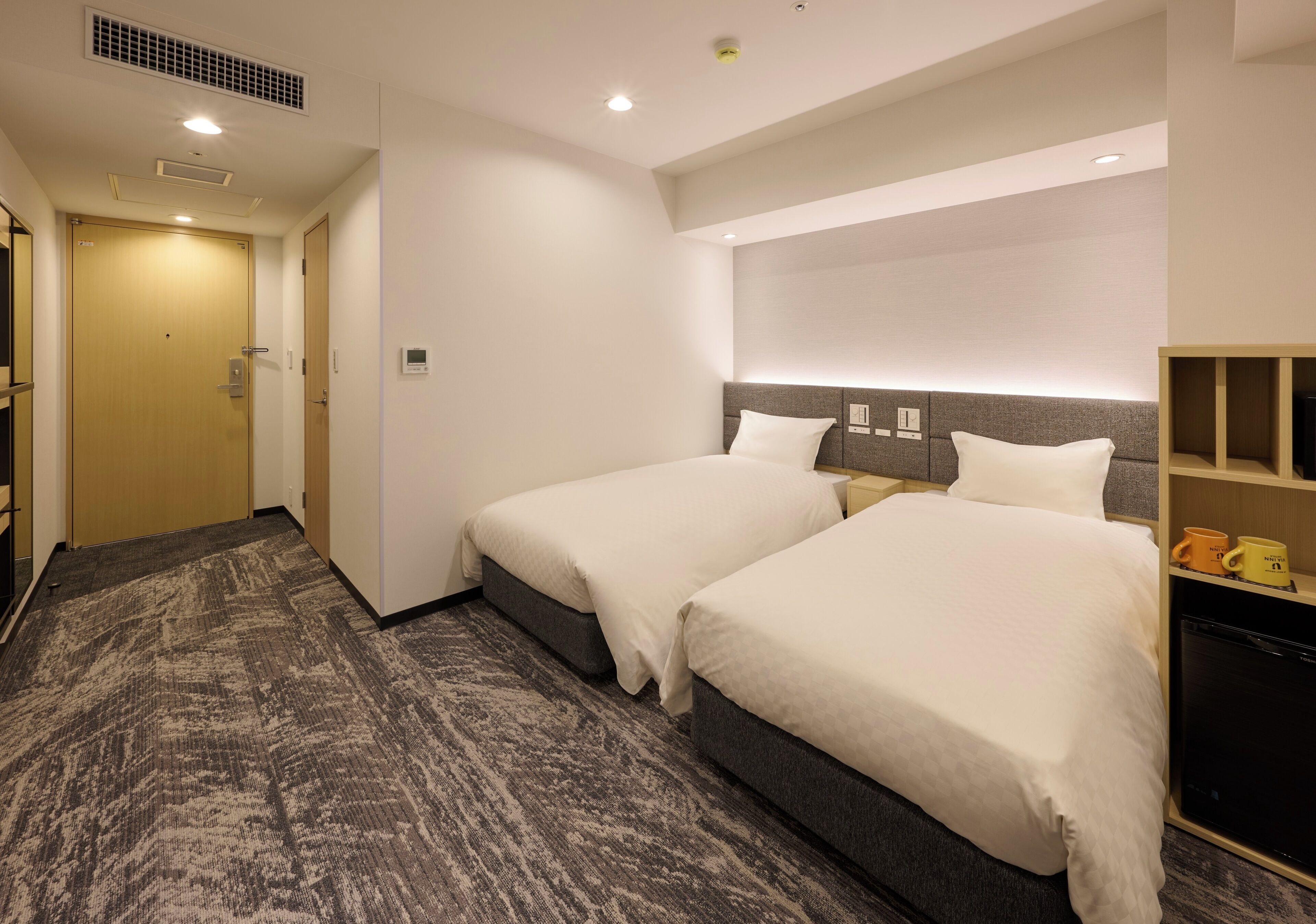 Habitación de hotel con dos camas, un escritorio pequeño, un armario y televisión integrada.