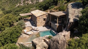 A stone villa with a swimming pool, outdoor seating, and a view of the surrounding forest.