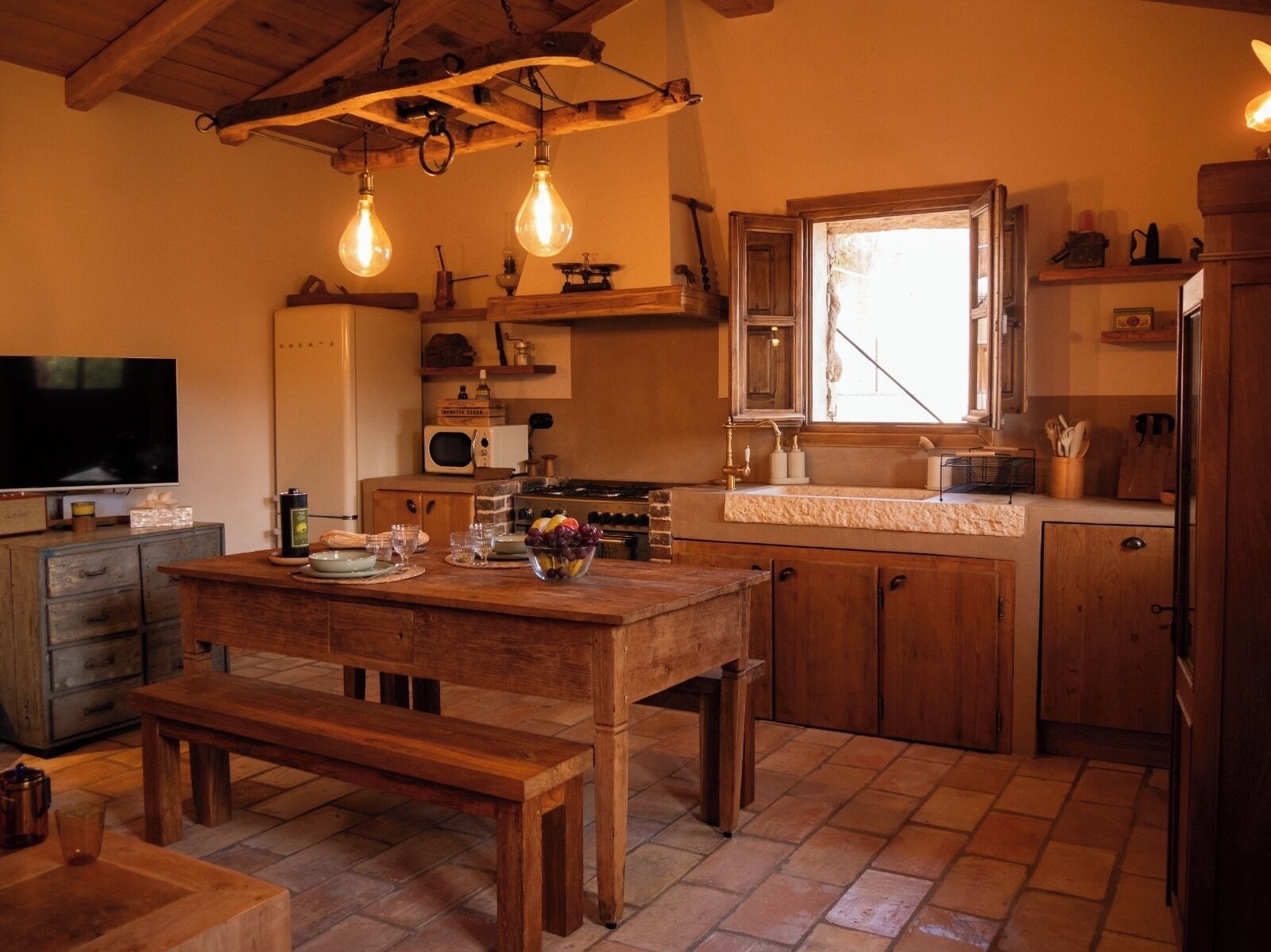 A rustic kitchen with wooden cabinets, a wooden dining table, a bench, and hanging light bulbs.