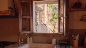 A kitchen with a stone countertop, a sink, a window with a view of a stone wall and greenery, and wooden cabinets.