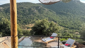 Une terrasse en bois avec une piscine à fond de verre, des chaises longues et une vue sur un paysage montagneux.
