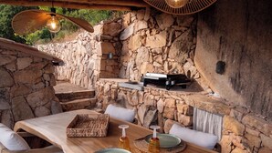 An outdoor dining area with stone walls, wooden furniture, and a grill.