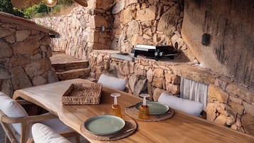Un espace extérieur aménagé pour les repas, avec des murs en pierre, du mobilier en bois et un barbecue.