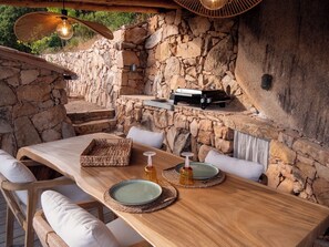 An outdoor dining area with stone walls, wooden furniture, and a grill. - Charming sheepfold in Corsica, heated pool, between scrubland and beautiful beaches. (Figari)