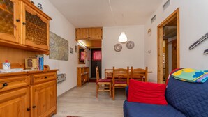 Ein gemütliches Zimmer mit einem Holzkasten, einem blauen Sofa, einem roten Kissen und einer Essecke mit einem Holztisch und Stühlen.