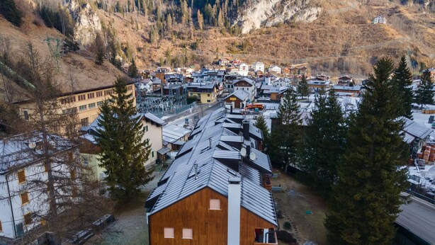 Ein modernes Gebäude mit Holzfassade, umgeben von einer gebirgigen Landschaft und anderen Wohnhäusern.
