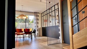 Un intérieur moderne avec un escalier en bois, un coin repas avec des chaises rouges et une vue à travers une porte vitrée.