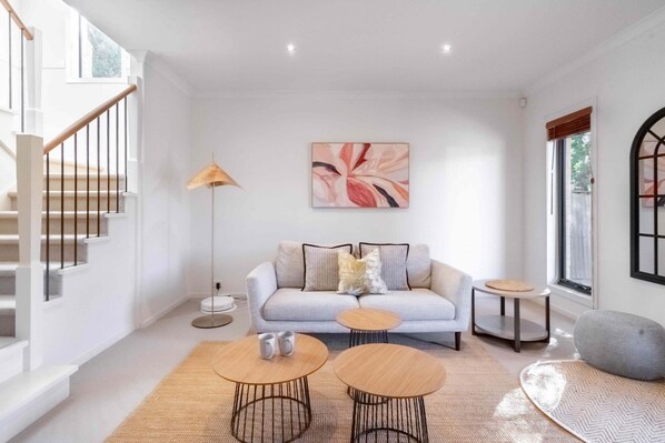 Ein modernes Wohnzimmer mit einer Couch, zwei runden Couchtischen, einer Stehlampe und einem großen, abstrakten Gemälde an der Wand.