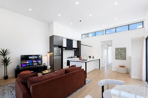 Ein modernes Wohnzimmer mit Fernseher, einer Couch und einer Küchenzeile inklusive Kühlschrank und Schränken.