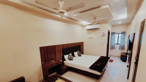 A hotel room with a bed, a small sofa, a wooden coffee table, a ceiling fan, an air conditioning unit, and a TV. - Aman Hotel (Pindra)