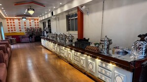 A long buffet table with food service stations, a chandelier, and a row of cushioned seating on the left. - Aman Hotel (Pindra)