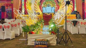 An outdoor event stage with a floral backdrop, a blue sofa, and a table with a floral arrangement. - Aman Hotel (Pindra)
