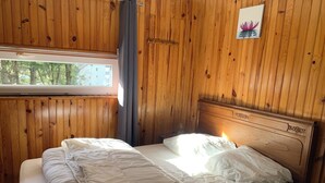 Habitación con paneles de madera, una cama, un ventanal y un cuadro colgado en la pared con una flor de loto.