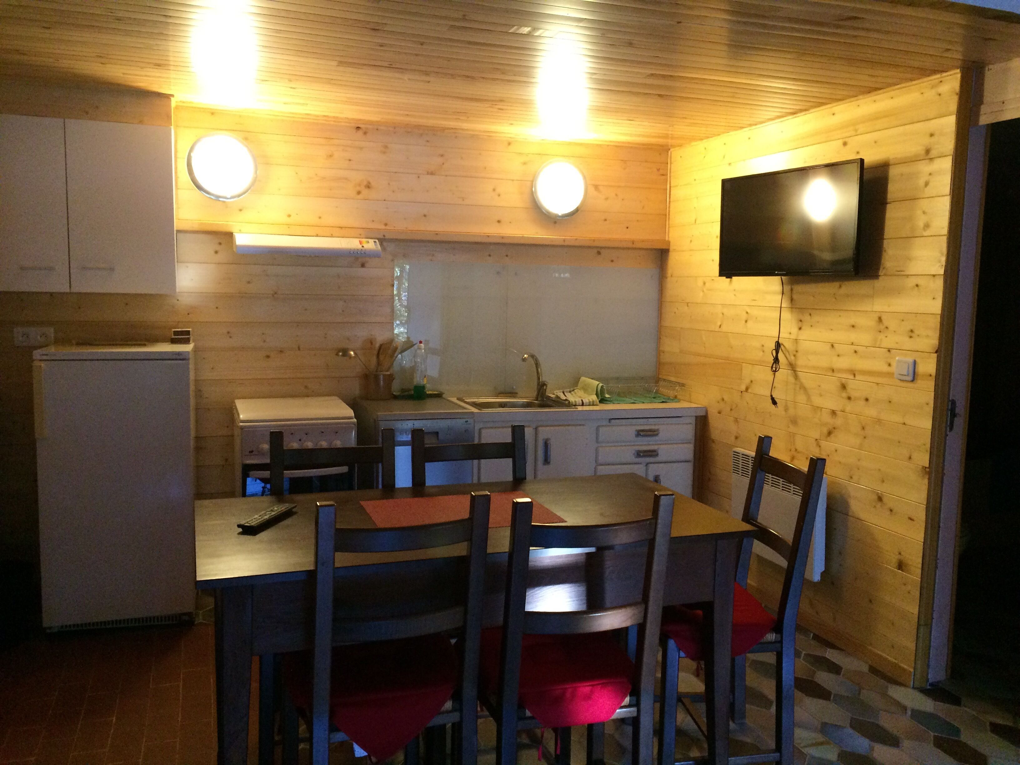 A compact kitchen with wooden walls, a built-in TV, and a dining area with chairs and a table.