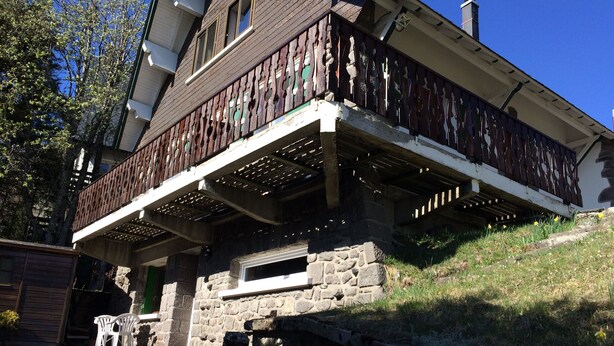 Una casa de dos pisos con base de piedra y un balcón de madera con barandilla ornamentada.