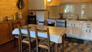 Cocina de cabaña de madera con mesa, sillas, estufa, refrigerador y armarios.