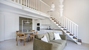 En rummelig opholdsstue med sofa, spisebord, stole og et køkken i baggrunden.